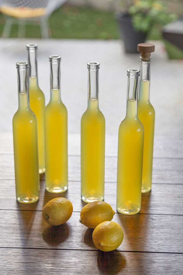 Bottles of homemade limoncello ready to be corked with lemons in the foreground. 