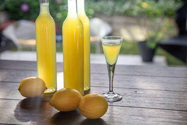 Three bottles of homemade limoncello with lemons and cocktail glass. 