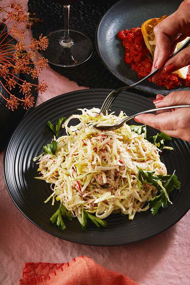 A person begins to serve a fennel and cabbage salad. 