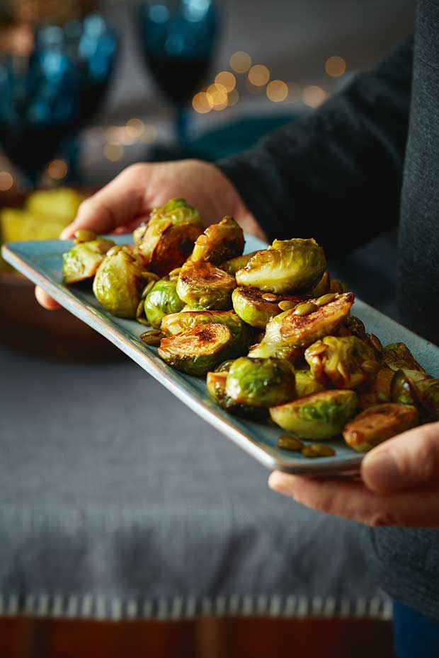 A person carries a long plate with honey roasted brussels sprouts and pepitas. 