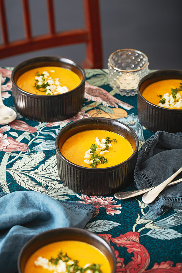Four pretty bowls of butternut and orange suit are on display with feta on top, surrounded by a funky tablecloth. 