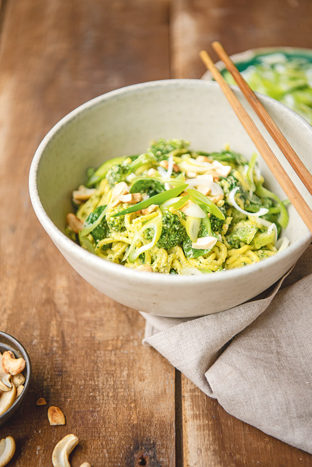 A bowl of noodles with coriander and fresh winter greens, with a pair of chopsticks resting on top. 